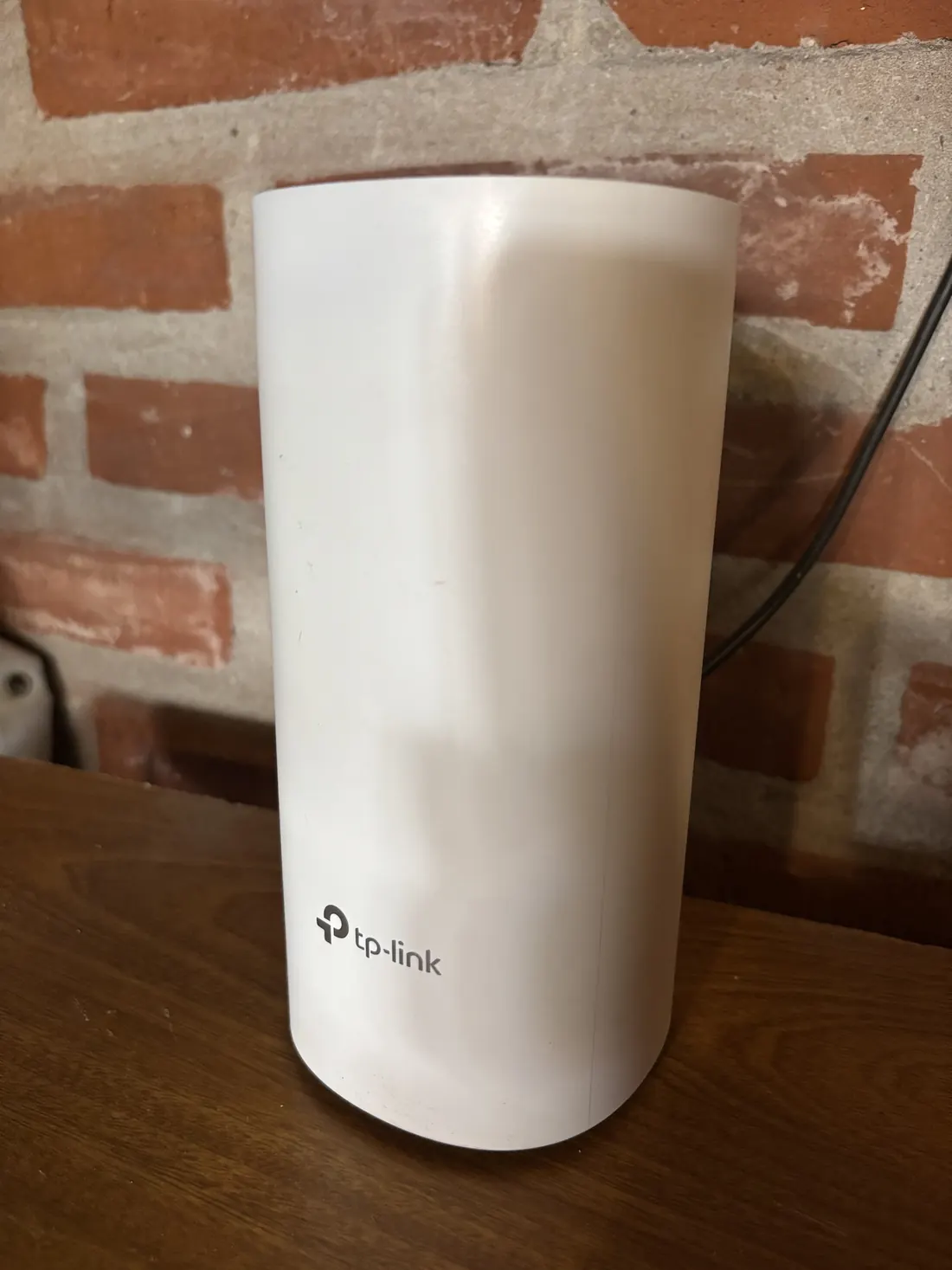 Nodo Deco de TP-Link sobre un mueble, frente a una pared de ladrillo